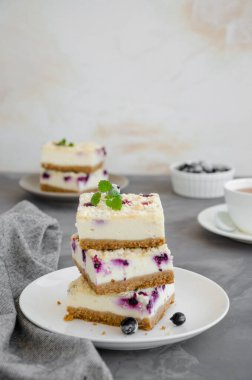 Siyah frenk üzümlü cheesecake ve beyaz bir tabakta çırılçıplak, koyu beton arka planda bir fincan çay. Frenk üzümlü kek. Lezzetli tatlı. Dikey oryantasyon. Boşluğu kopyala