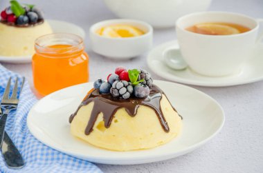 Süzme peynir güveci ya da çikolata soslu puding ve beyaz tabağın üstünde hafif arkaplanda bir fincan çayla birlikte böğürtlen. Sağlıklı kahvaltı. Yatay oryantasyon. Kapat.