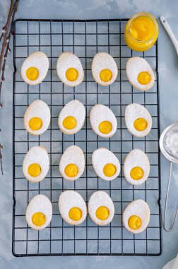 Paskalya yumurtası şeklinde paskalya kurabiyeleri, açık mavi beton zemin üzerinde pudra şekeri ve limon kreması. Dikey oryantasyon, kapat. Üst görünüm