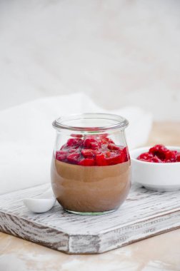 Italian dessert - chocolate panna cotta, mousse, cream or pudding with cherry sauce in a glass jar on a board on a light concrete background. Vertical orientation. Copy space. clipart