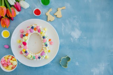 Paskalya pastası yumurtası krema, şeker yumurtası, kurabiye, krema ve üzerine açık mavi arka planda bir buket lale ile serpiştirilmiş şekerlemeler. Paskalya kartı. Paskalya pastası. Yatay, üst görünüm, boşluğu kopyala