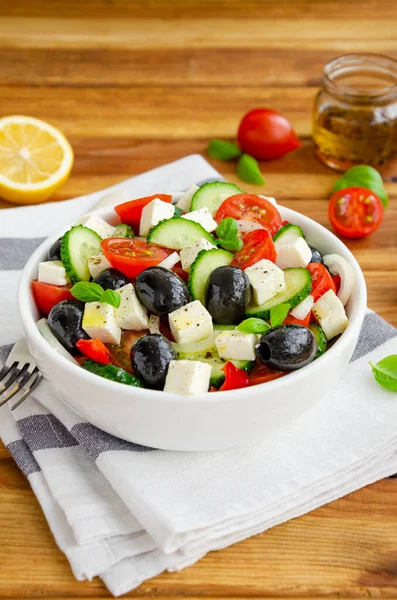 Greek salad of fresh juicy vegetables, feta cheese, herbs and olives in a white bowl on a wooden background. Healthy food. Vertical orientation
