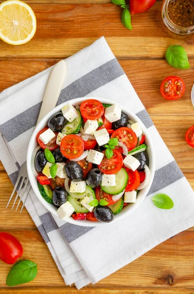Yunan salatası taze meyve suyu, peynir, otlar ve zeytinler ahşap arka planda beyaz bir kasede. Sağlıklı yiyecekler. Dikey oryantasyon. Üst görünüm