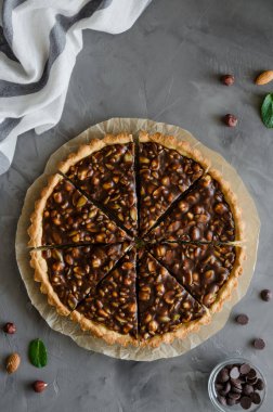 Çikolatalı karamelli tart, fındık, fıstık, badem ve tohum karışımı koyu beton bir arka planda. Dikey oryantasyon. Üst görünüm