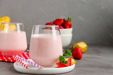 Çilekli smoothie veya muzlu milkshake gri beton arka planda. Soğuk yaz içeceği. Yatay oryantasyon. Boşluğu kopyala