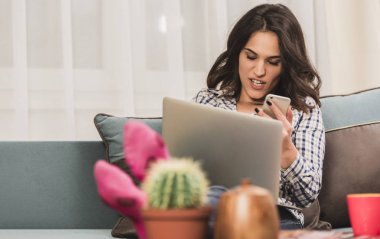 güzel esmer siting, cep telefonuyla konuşan ve bir dizüstü bilgisayarda aynı anda sohbet kanepe.