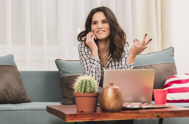 güzel esmer siting, cep telefonuyla konuşan ve bir dizüstü bilgisayarda aynı anda sohbet kanepe.