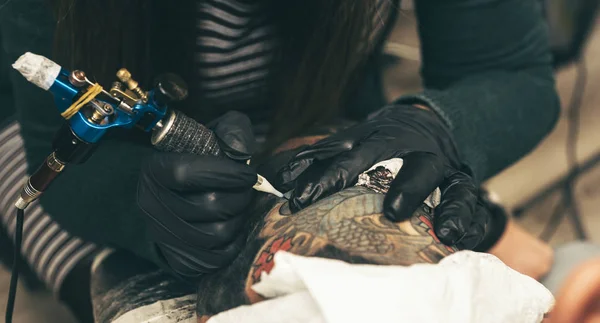 tattoo artist makes a picture of a woman in a black gloves and a blue shirt.