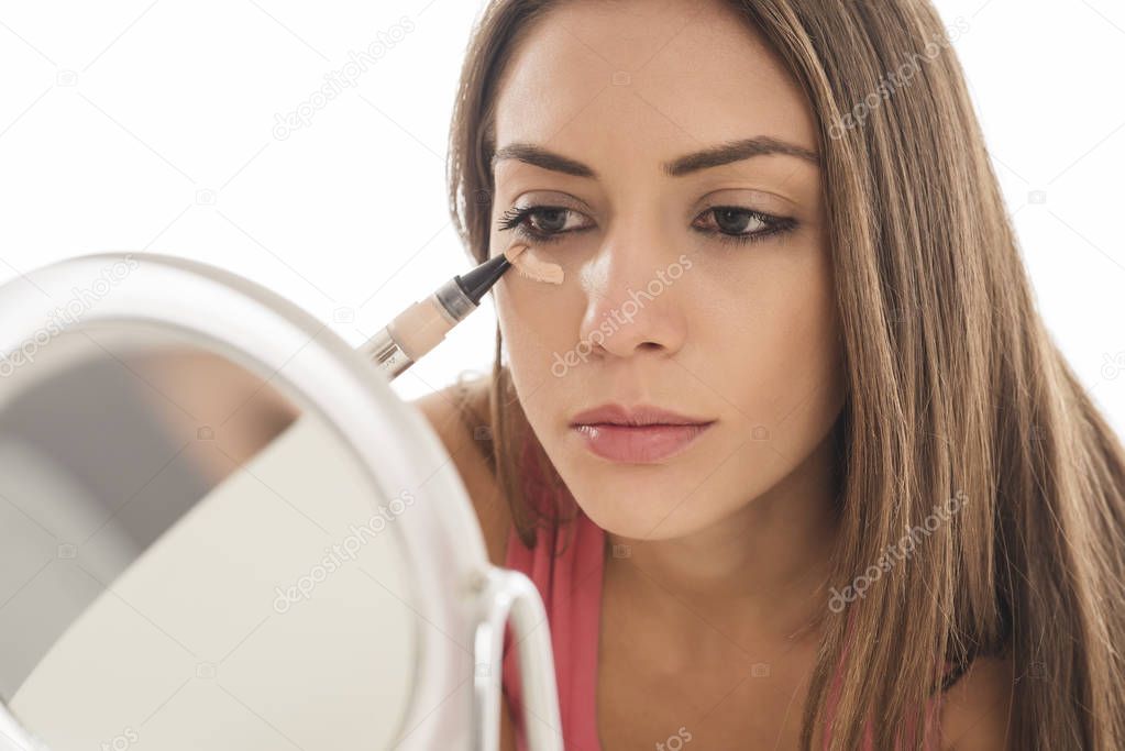  young woman applies a concealer under the eyes. isolated on white background