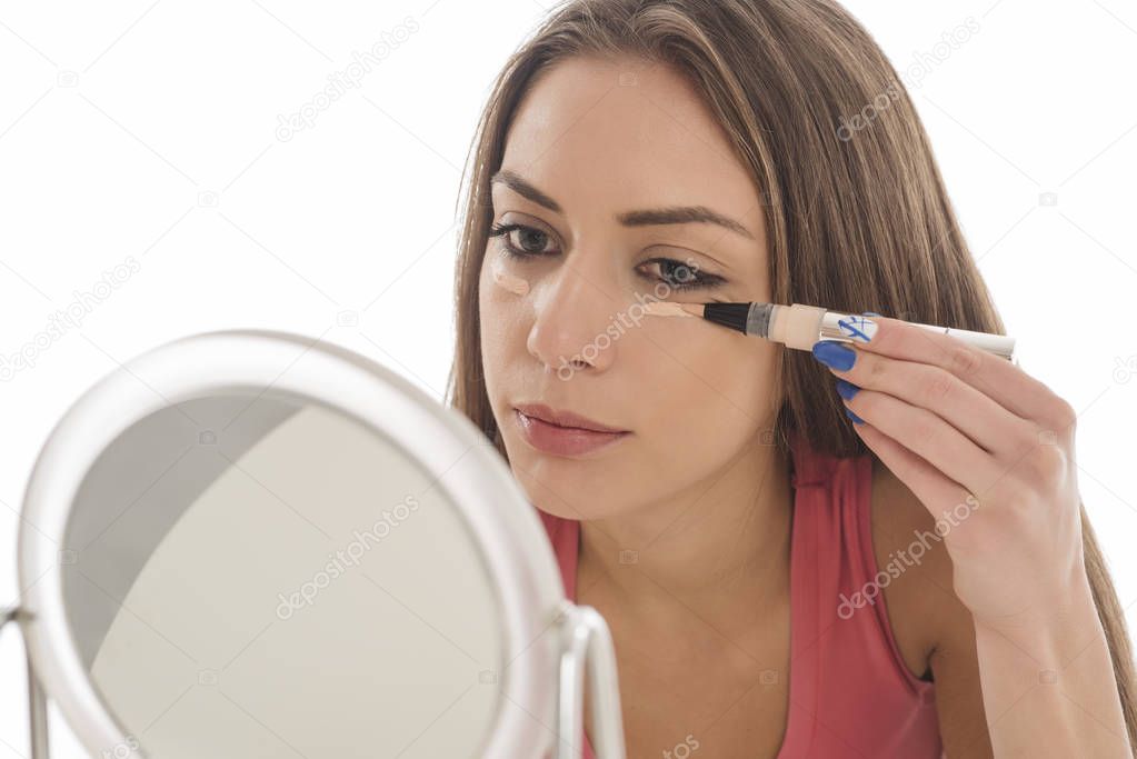  young woman applies a concealer under the eyes. isolated on white background