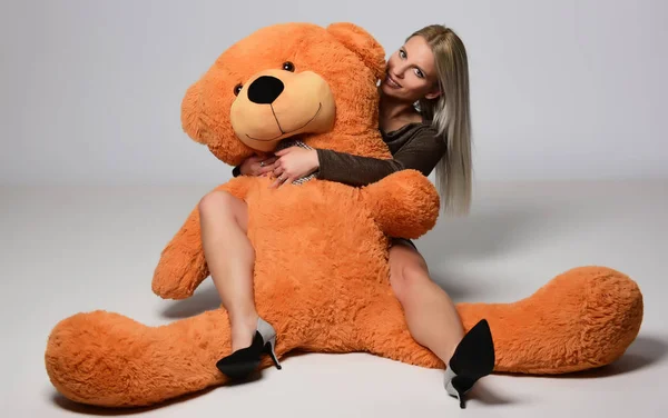 Portrait of beautiful blonde woman hugging big teddy bear posing in studio