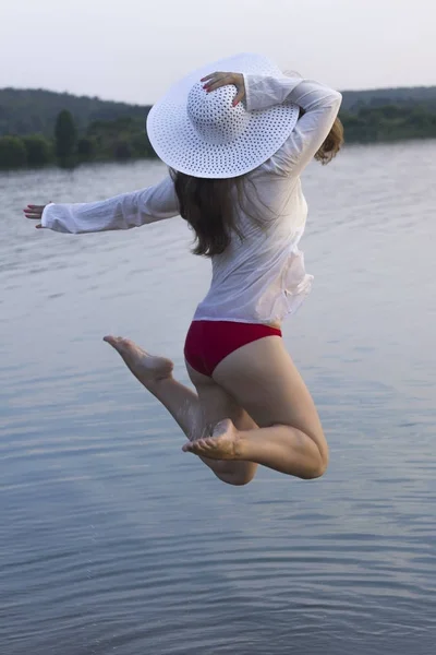 white woman in sun hat jump in water