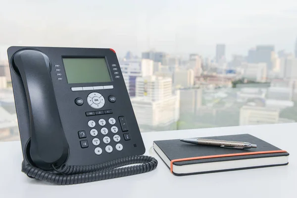 IP Phone and notebook with pen on the white office desk