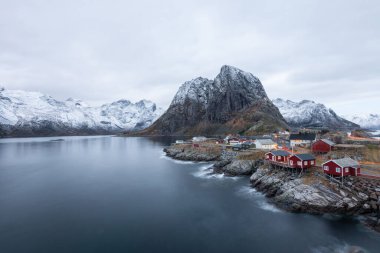 Lofoten adası Hamnoy Norveç 'te dağ manzaralı karların arasında kırmızı balıkçı köyü