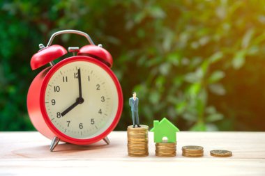 Para biriktirme konsepti için küçük insan ve evle bozuk para yığını ve saat büyütmek