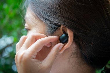 Kadın kulaklığı takmak ve kontrol etmek için siyah, gerçek, kablosuz kulaklıkları elle kullanıyor.