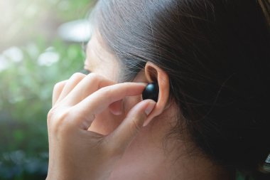 Kadın kulaklığı takmak ve kontrol etmek için siyah, gerçek, kablosuz kulaklıkları elle kullanıyor.