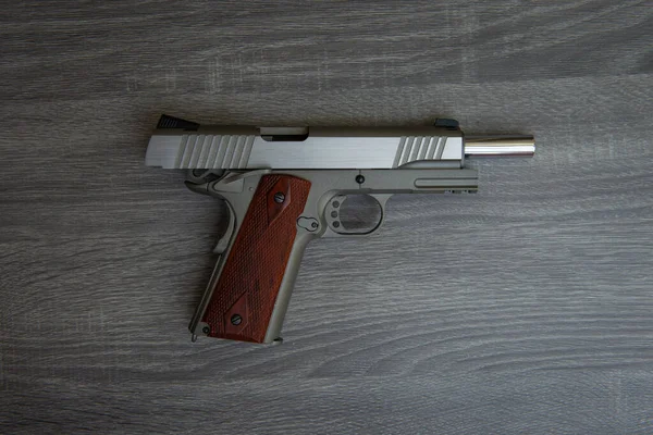 Stainless hand gun with brown hand grip is on the wooden floor  - begun slide on