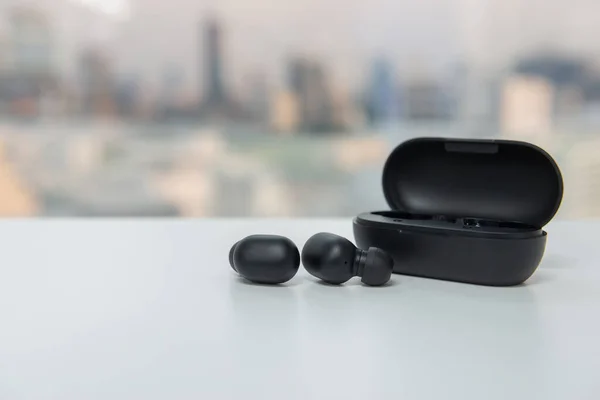 True wireless earbuds with battery case on the white table with blur city scape background