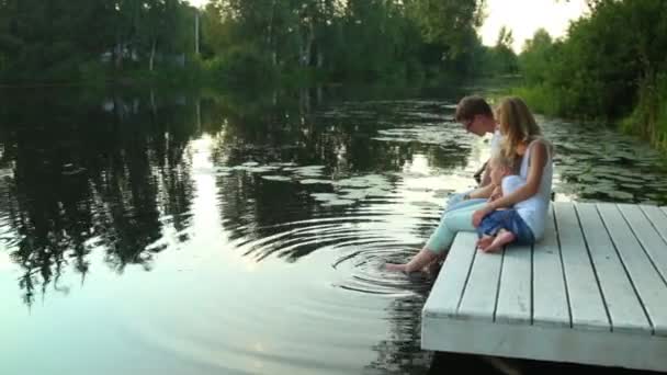 Οικογένεια κάθεται δίπλα στη λίμνη, περιβάλλεται από πράσινο της φύσης — Αρχείο Βίντεο