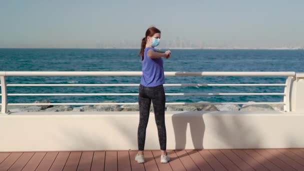 Fille portant un masque médical et fait des exercices près de la mer — Video