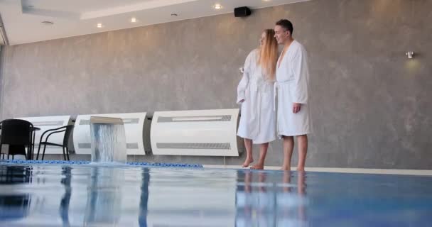 Pareja romántica en batas blancas abrazos de pie en el borde de la piscina — Vídeo de stock