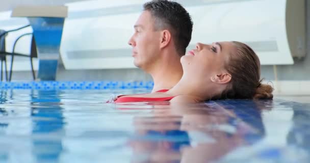 Ung kvinde i badedragt driver på swimmingpool vand af mand – Stock-video