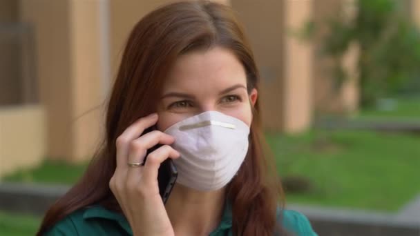 Дівчина в медичній масці розмовляє по телефону — стокове відео