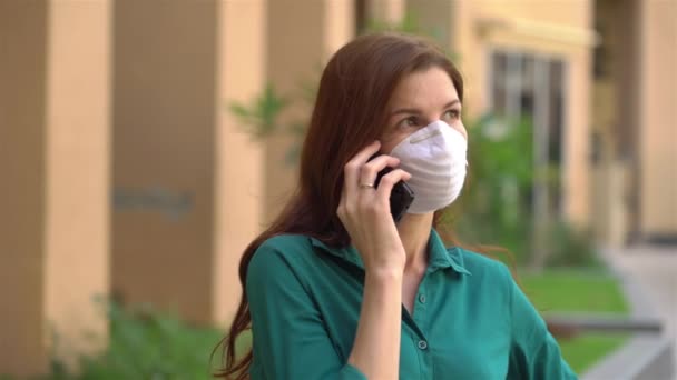 Дівчина в медичній масці розмовляє по телефону — стокове відео