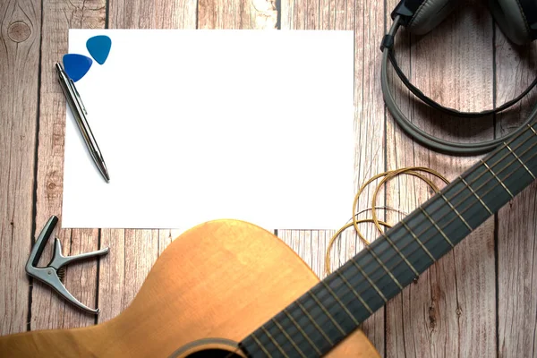 Some of the acoustic guitars have blank paper, pen, blue Guitar pick. Capo headphones on a wooden floor