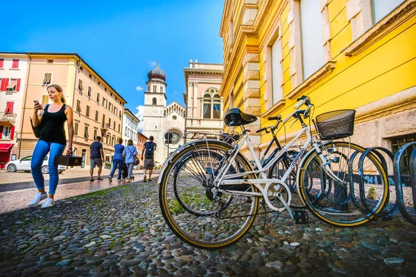 Fahrräder, die in der Nähe der Kathedrale von Trento geparkt sind, ein Mädchen geht spazieren, während sie auf ihr Smartphone schaut - Trento, — Stockfoto