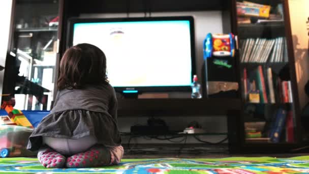 Новонароджена дитина дивитися телевізор на килимі у вітальні шкарпетки вид ззаду — стокове відео
