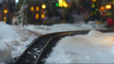 Noel oyuncağı tren modeli. Arka planda kasaba ışıkları olan karların üzerindeki rayları kapat.