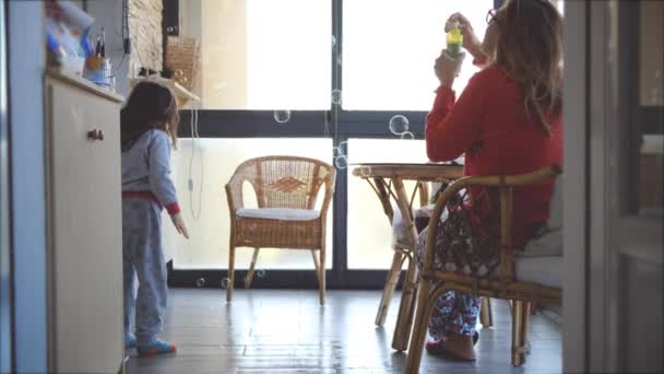 Mutter Kinder Tochter bleibt zu Hause zusammen - Mama pustet Seifenblasen unterhalten Baby Mädchen lachen Sprungtanz auf lustige komische Weise — Stockvideo