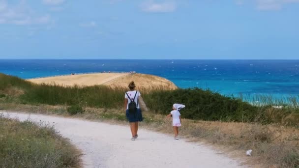 地中海の海の背景につながる歩道を歩く母親と赤ん坊の女の子 — ストック動画