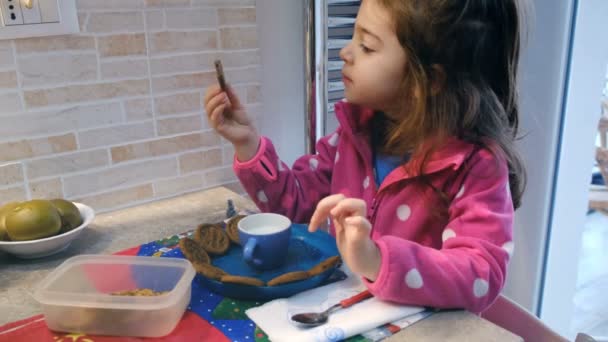 เด็กสาวอายุสี่ขวบทานอาหารเช้ากับนมและบิสกิตในครัวที่บ้าน — วีดีโอสต็อก