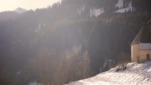 Berglandschap sneeuw helling met kerk in de winter 's morgens met zonnevlam en lens flare — Stockvideo