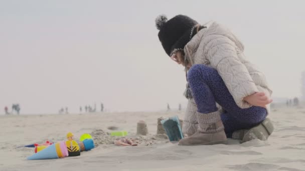 Liten flicka leka med sand på stranden i en vinter blek morgon ljus — Stockvideo