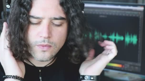 Kompozytor muzyki człowiek z długimi włosami słuchać ze słuchawkami koncentrując się z oprogramowania audio histogram w tle ekranu PC — Wideo stockowe