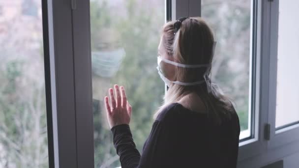 Kvinna vid fönstret med en mask isolerad för virusutbrott — Stockvideo