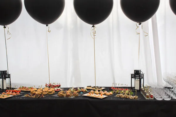 Различные закуски на черном столе и воздушные шары — стоковое фото