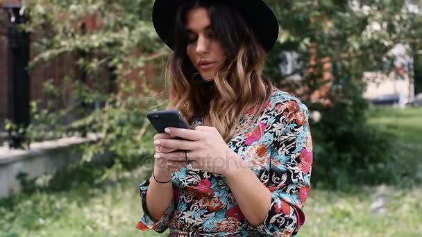 A menina com um smartphone na cidade em um chapéu — Vídeo de Stock