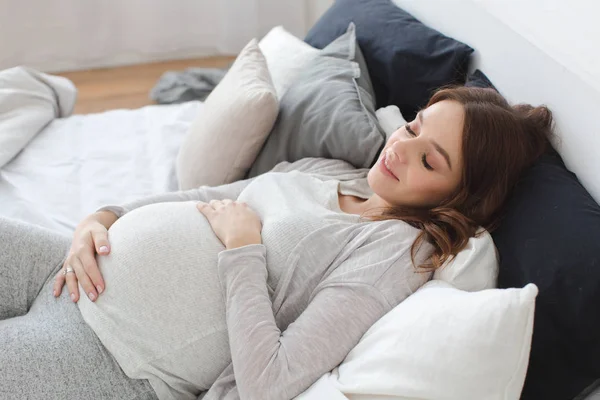 W ciąży, uśmiecha się kobieta leżąc na łóżku — Zdjęcie stockowe