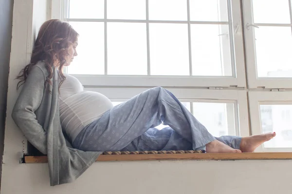 Mulher grávida está sentada no peitoril da janela — Fotografia de Stock