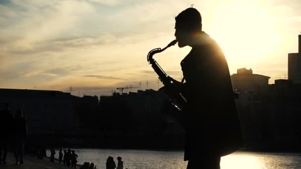 Straat muzikant Speel saxofoon zonsondergang silhouet — Stockvideo