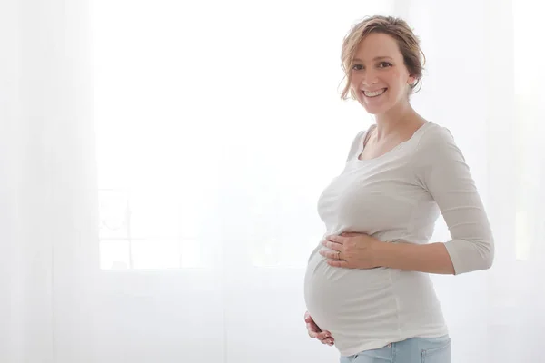 Pregnant woman touching belly looking at camera — Stock Photo, Image