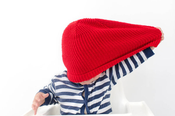 Toddler takes off hat in red cap over face studio