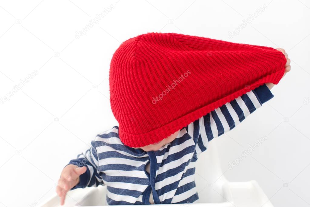 Toddler takes off hat in red cap over face studio