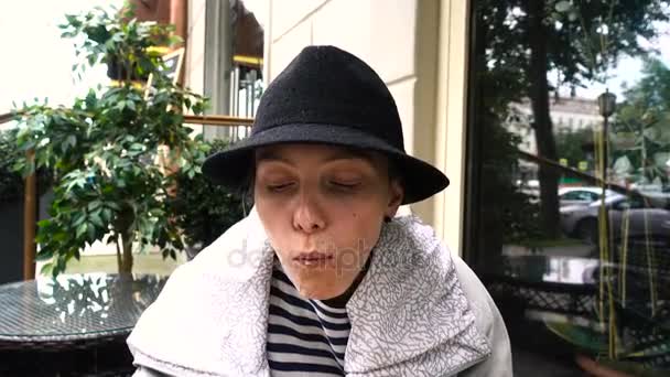 Женщина в шляпе ест гамбургер на улице — стоковое видео