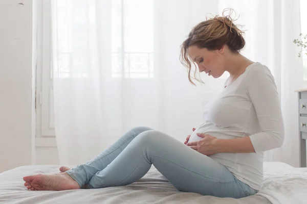 Pregnant woman sitting on bed looks at the belly — Stock Photo, Image